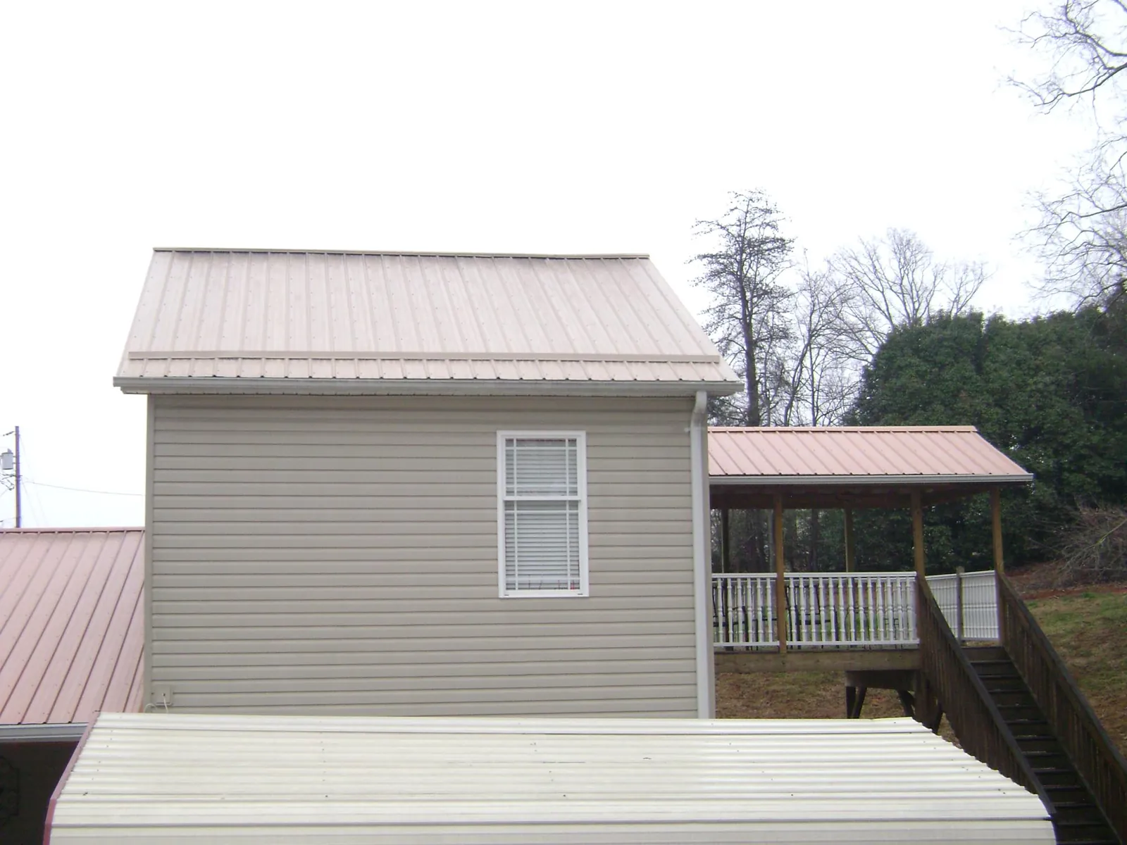 Tan metal roofs on a two story addition and attached porch, from a Roof Replacement job in Blanchard